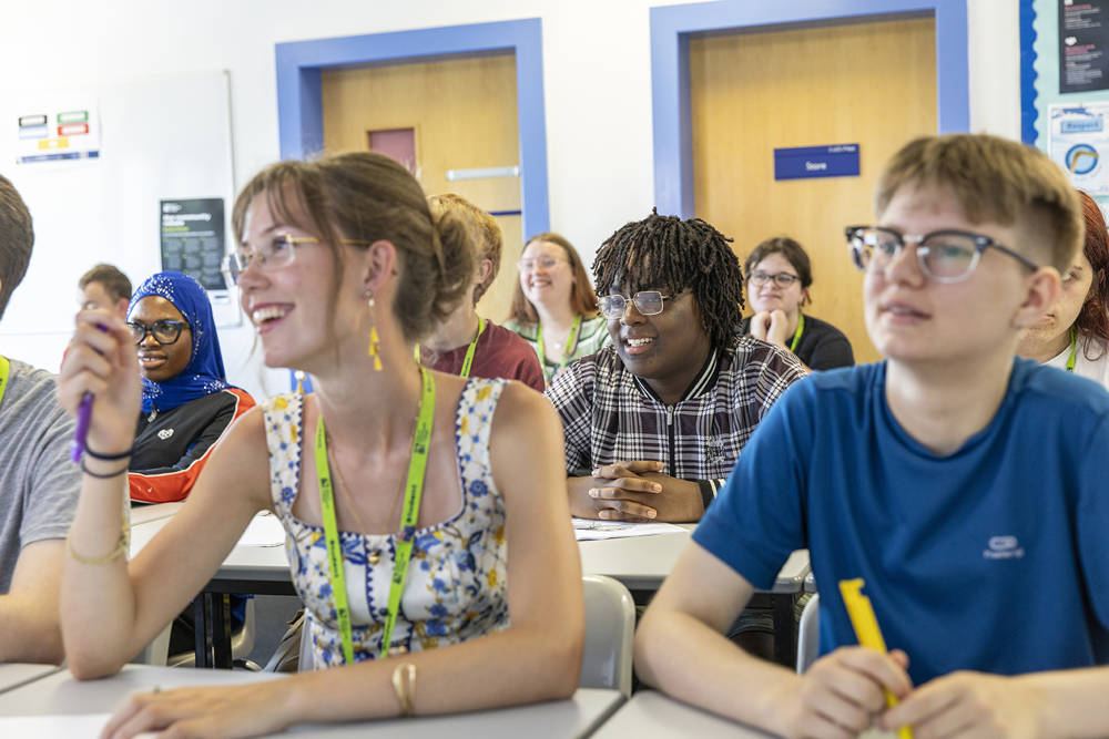 A close up image of COPC students in a classroom during class. They are sat att desks, smiling and engaging in the learning activity.