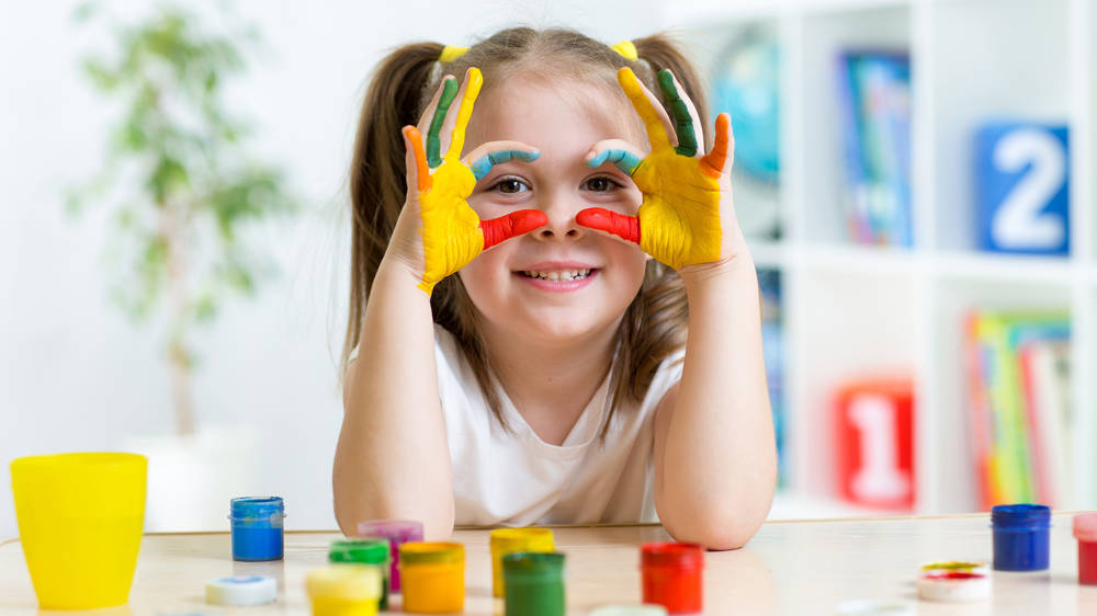 Cheerful young girl showing her hands painted in bright colours