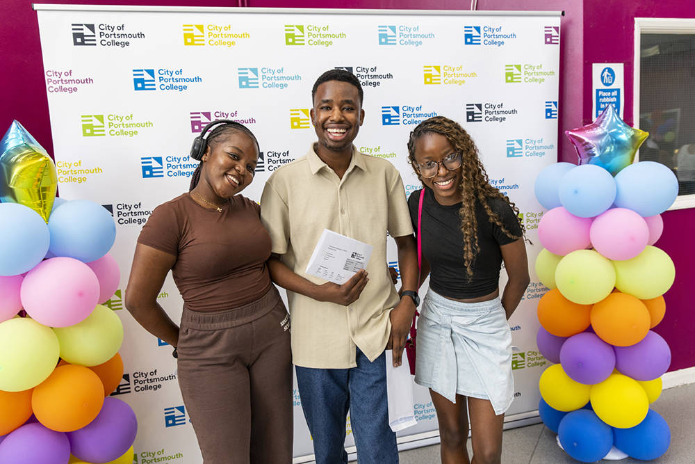 A City of Portsmouth College Sixth Form student with his family on A Level results day. They are stood against a backdrop with balloons and are all smiling.