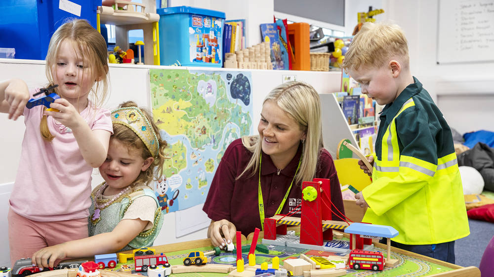 Student supporting young children during play based learning activities with toys and role play equipment in an early years setting.