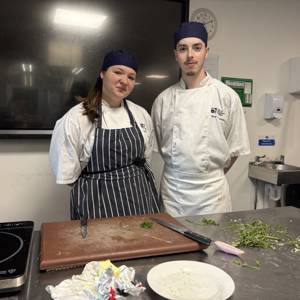Level 2 Diploma in Professional Cookery students Amelia Stuart, left, and Oliver Lewendon, right, posing in front of a food preparation station