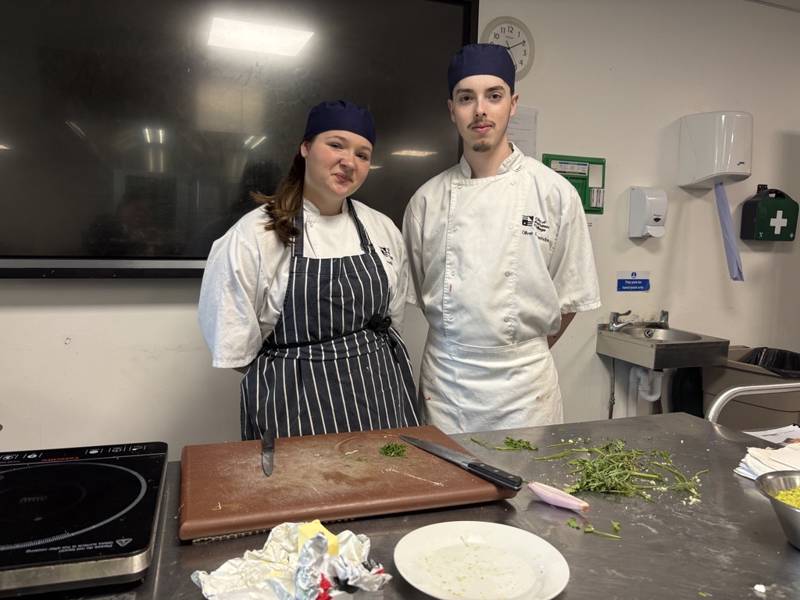 Level 2 Diploma in Professional Cookery students Amelia Stuart, left, and Oliver Lewendon, right, posing in front of a food preparation station