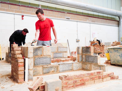 A student constructing a wall of breeze blocks in a bricklaying workshop 