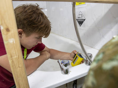 A plumbing student testing the water from a bath 