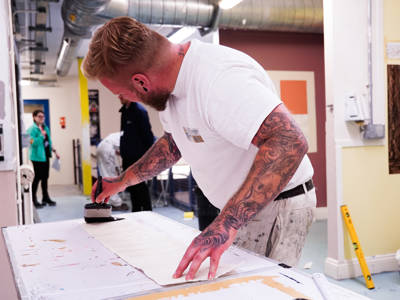 A male student applying adhesive to wallpaper 