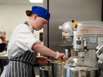 A student using an industrial mixer in a catering kitchen 