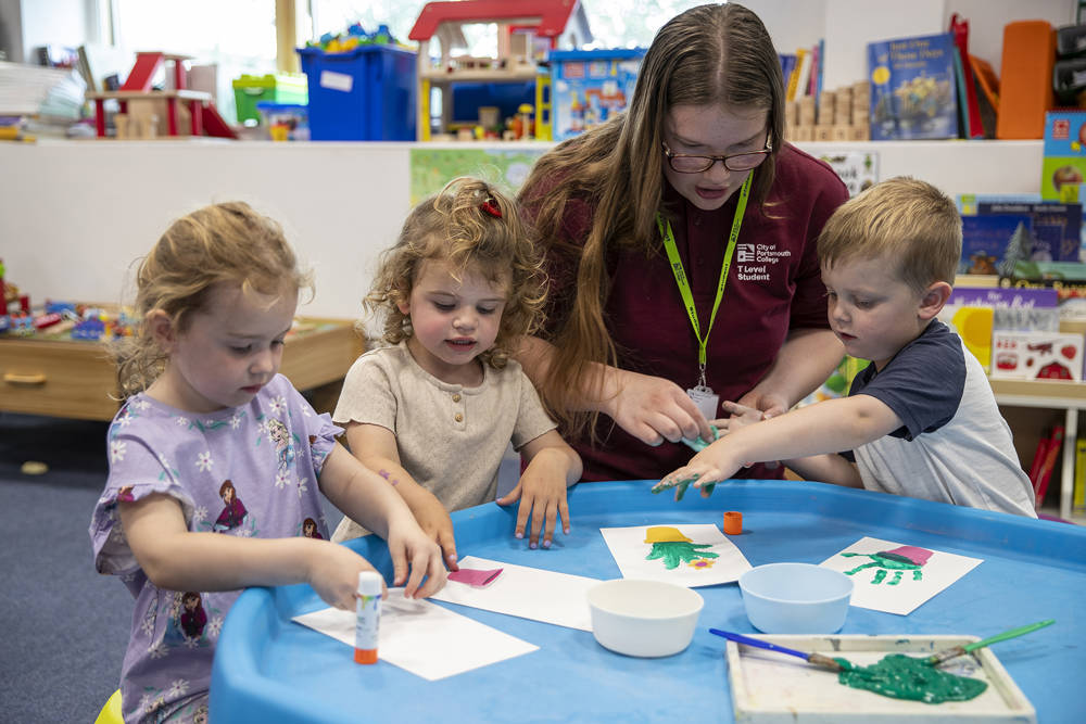 Student supporting young children with painting and craft activities in an early years classroom setting.