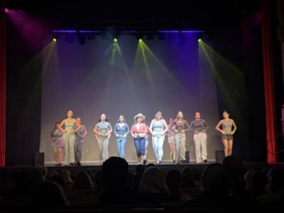 Maddison Woods plays Dolly Parton and performs a line dance with castmates on stage for Pinnacle