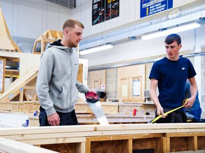 Two male carpentry students measuring and cutting wood in the workshop