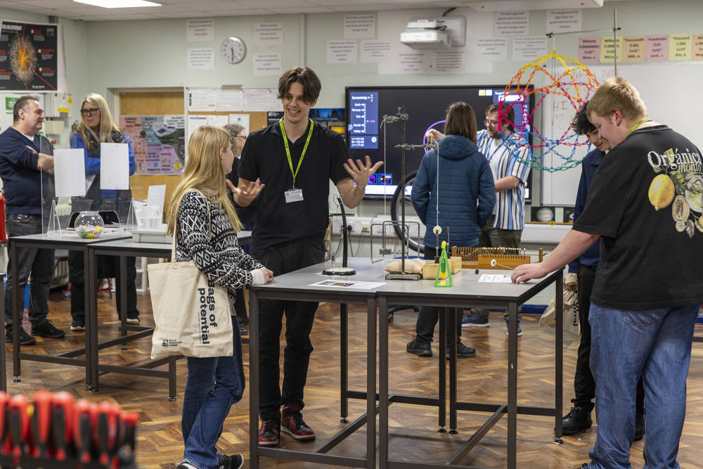 Student ambassador talking to a visitor at a City of Portsmouth College open event, with hands-on science displays in the classroom.