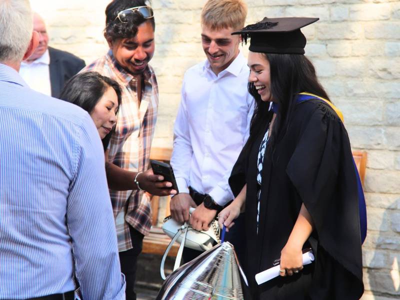 Graduate celebrating and taking selfie with family at Graduation ceremony.