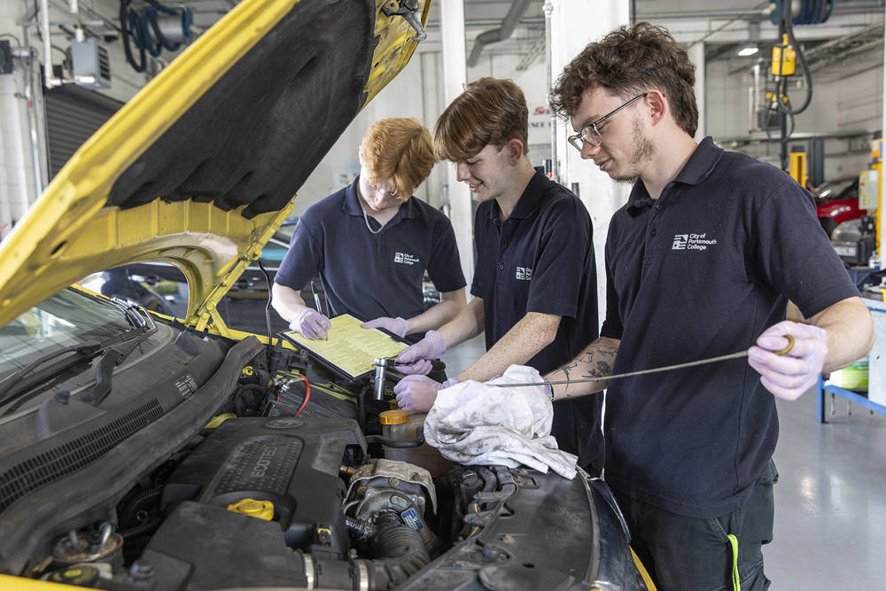 Three Automotive students working under the bonnet of a car checking oil levels.