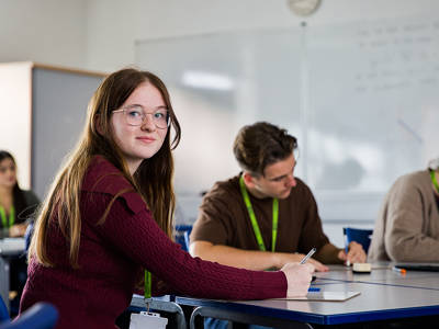 Student taking notes during a maths lesson while other students work at desks in the classroom.