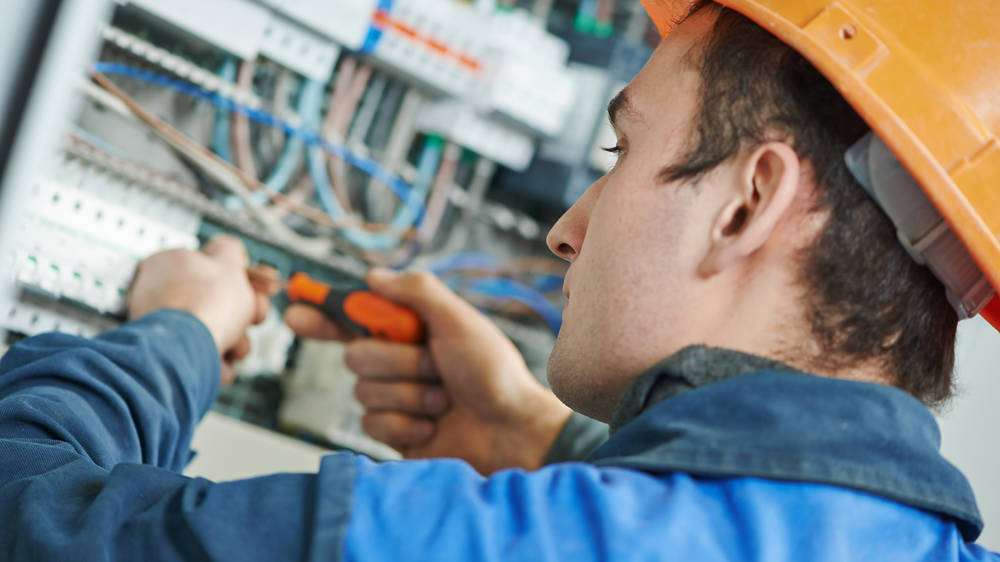 Young adult electrician builder engineer screwing equipment in fuse box
