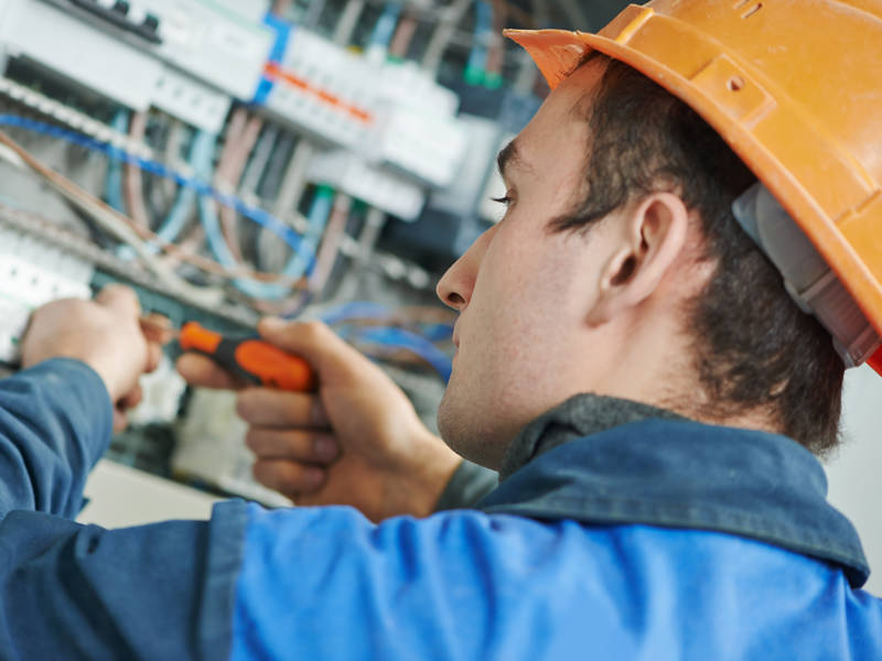 Young adult electrician builder engineer screwing equipment in fuse box