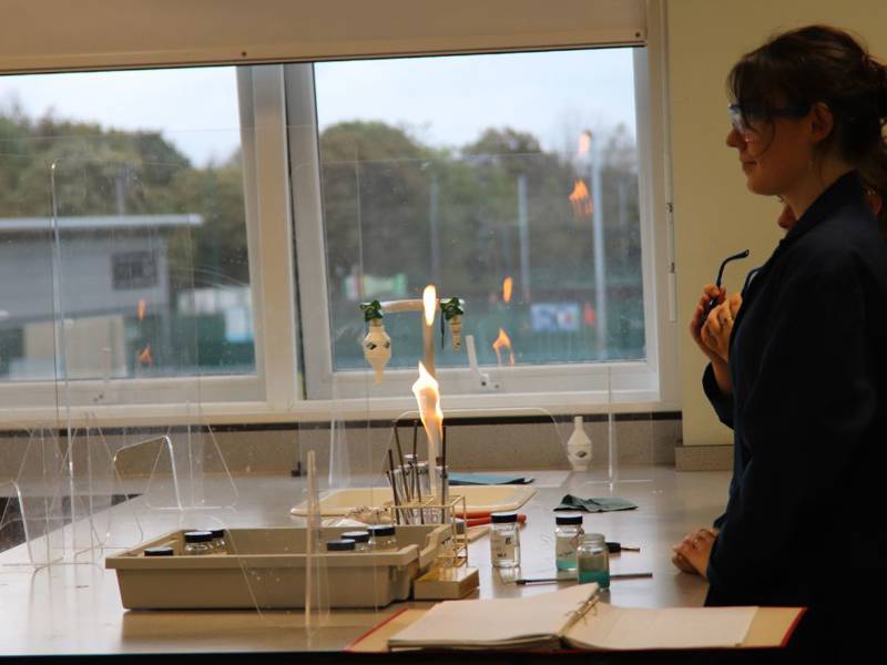 Student in lab coat with bunsen burner in Science lab.