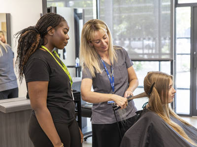 Hairdressing student observing a tutor straighten a client's hair at the Highbury Campus Retreat Salon