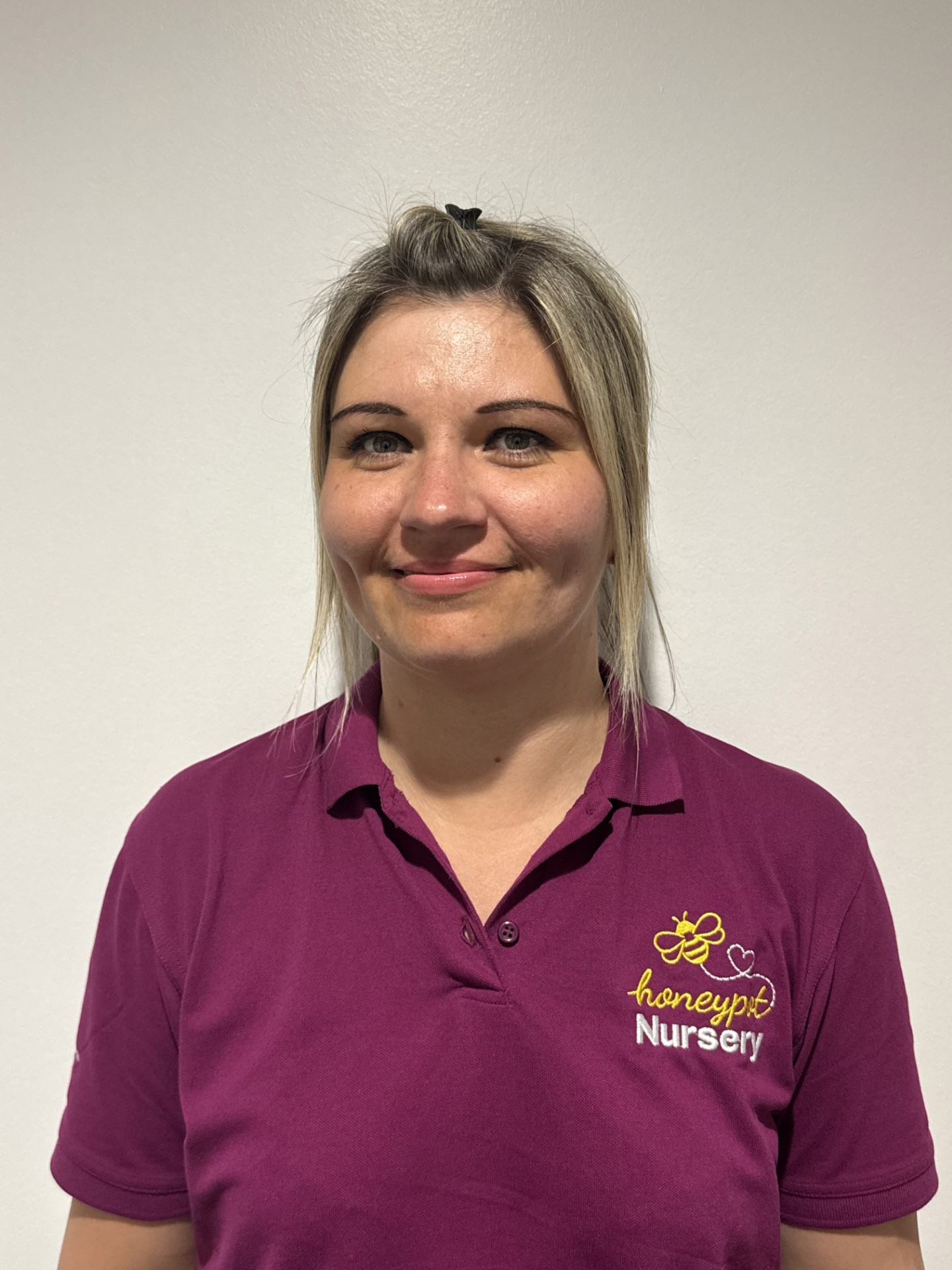 Portrait of Jo, Nursery Practitioner at Honeypot Nursery, smiling and wearing a purple uniform, with over 10 years’ experience supporting babies’ development and early learning.