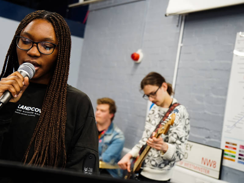 Female music technology student holding microphone in studio.
