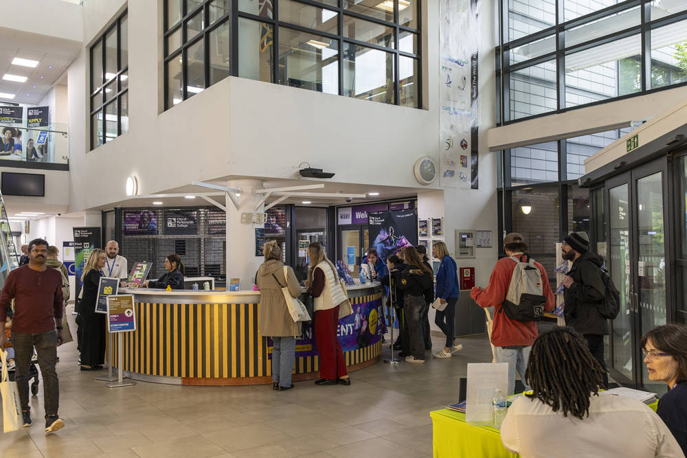Prospective students and families arriving at City of Portsmouth College Welcome Day and receiving information from staff in the main reception area.