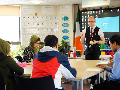Tutor leading an adult learning class with students working at tables in the classroom.