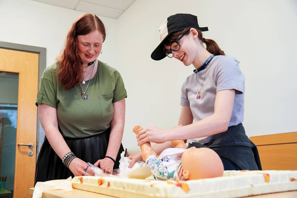 Two happy early years students training with baby mannequin