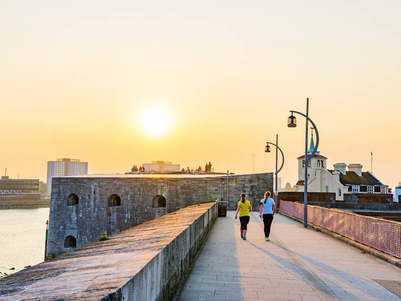 Two female walkers seen at Hotwalls in Old Portsmouth at sunset.