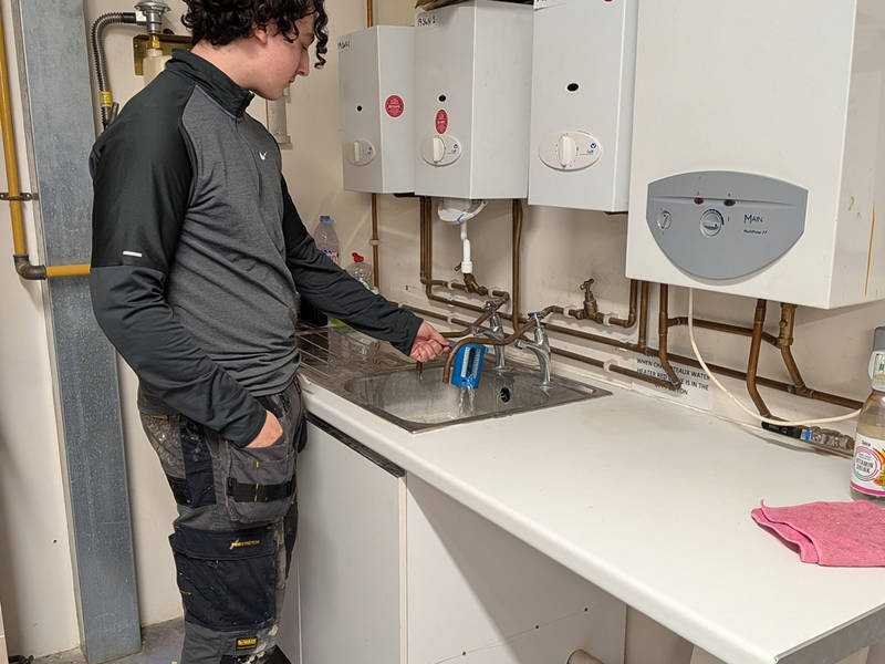 Engineer measuring water flow and temperature at a sink during Water Regulations training.