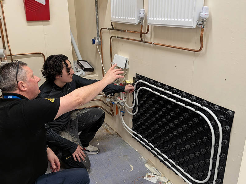 Tutor demonstrating central heating controls, radiators and underfloor heating system during energy efficiency training for gas engineers.