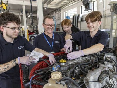 Automotive students and tutor working on a car engine in the College workshop