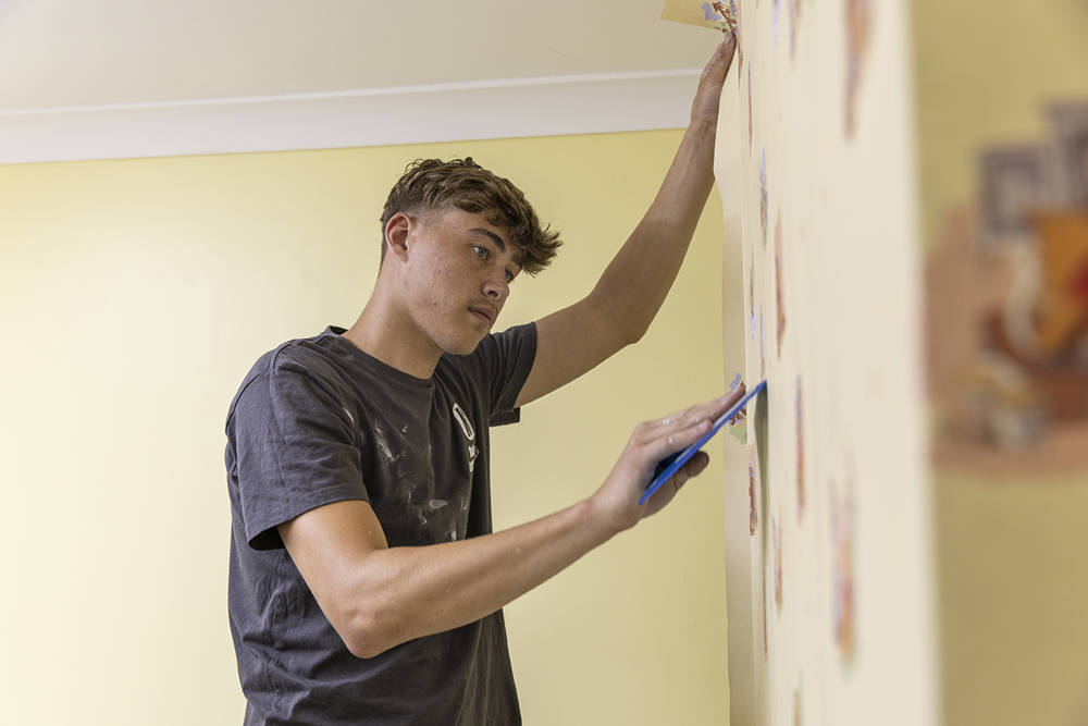 A COPC apprentice applying wallpaper in a clients home.