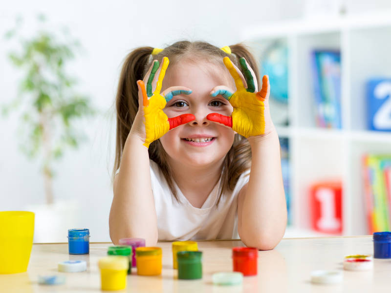 Cute cheerful girl showing her hands painted in bright colours